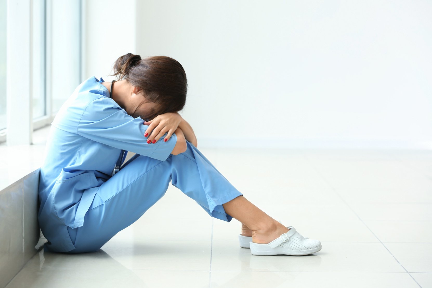 Tired Female Nurse Sitting on Floor in Hospital